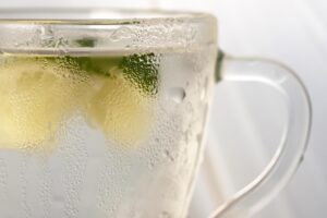 Bicchiere di acqua calda con limone su un tavolo, simbolo di benessere mattutino.